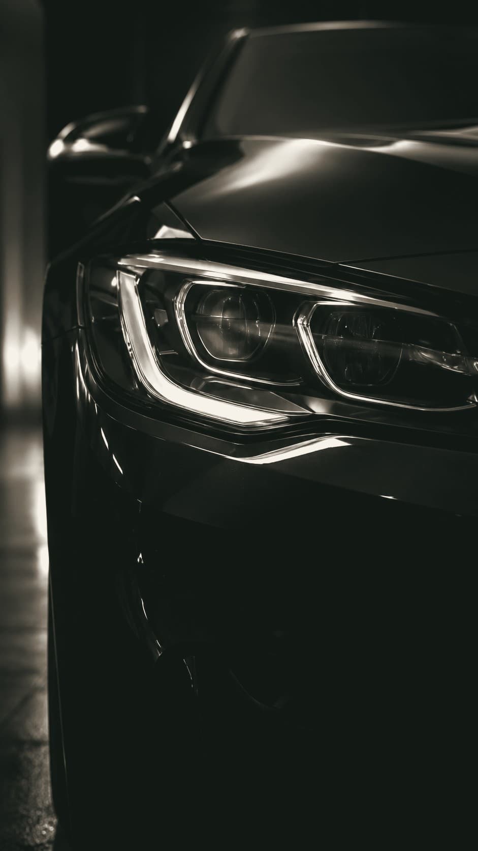 The sculpted headlight of a black coupe under low studio light